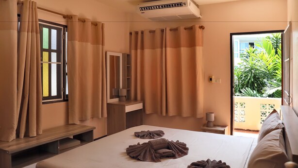 A hotel room with a bed, a bedside table, a mirror, a window with curtains, and an air conditioning unit. - Villa Kamala Beach (Kamala)