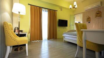 Una habitación con una cama, dos sillones amarillos, una mesa, una lámpara, un televisor y una ventana con cortinas.
