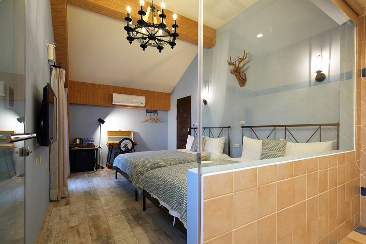 A bedroom with a bed, a chandelier, a mounted deer head, and a bathroom with tiled walls.