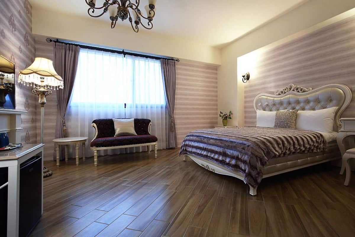 A spacious bedroom with a large bed, a sitting area with a sofa and armchairs, a small table, and a chandelier.