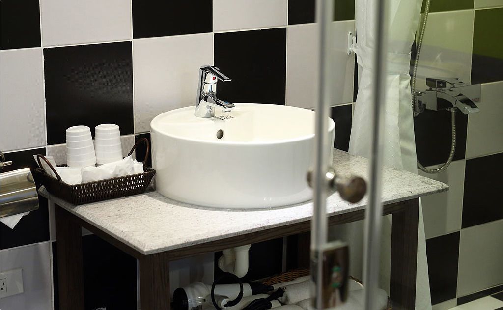 A bathroom with a white sink, a glass shower enclosure, and a black and white tiled wall.