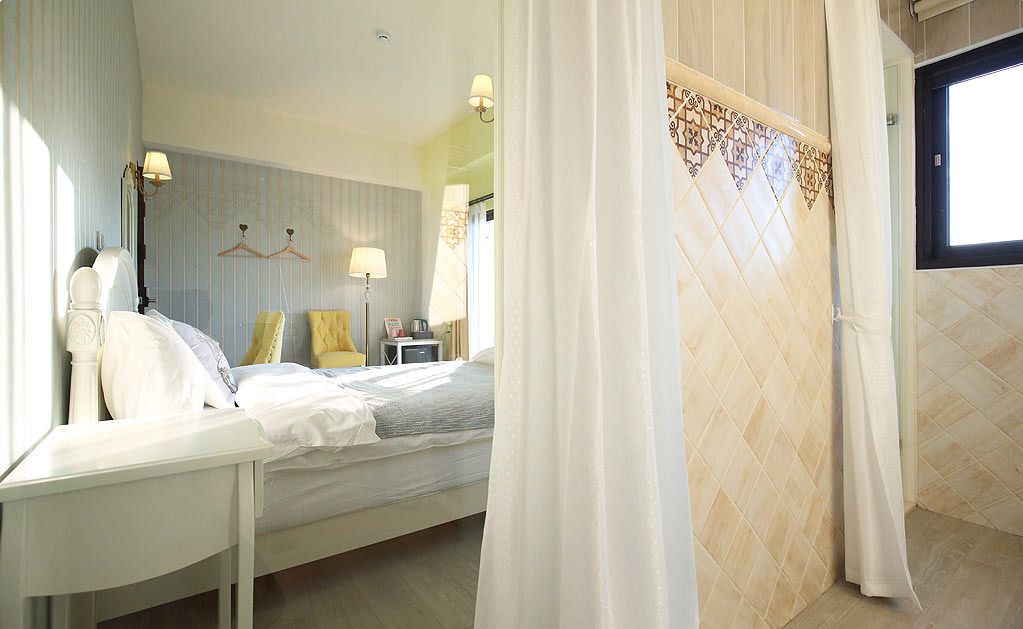 A hotel room with a bed, bedside table, lamp, and a view of the outside.