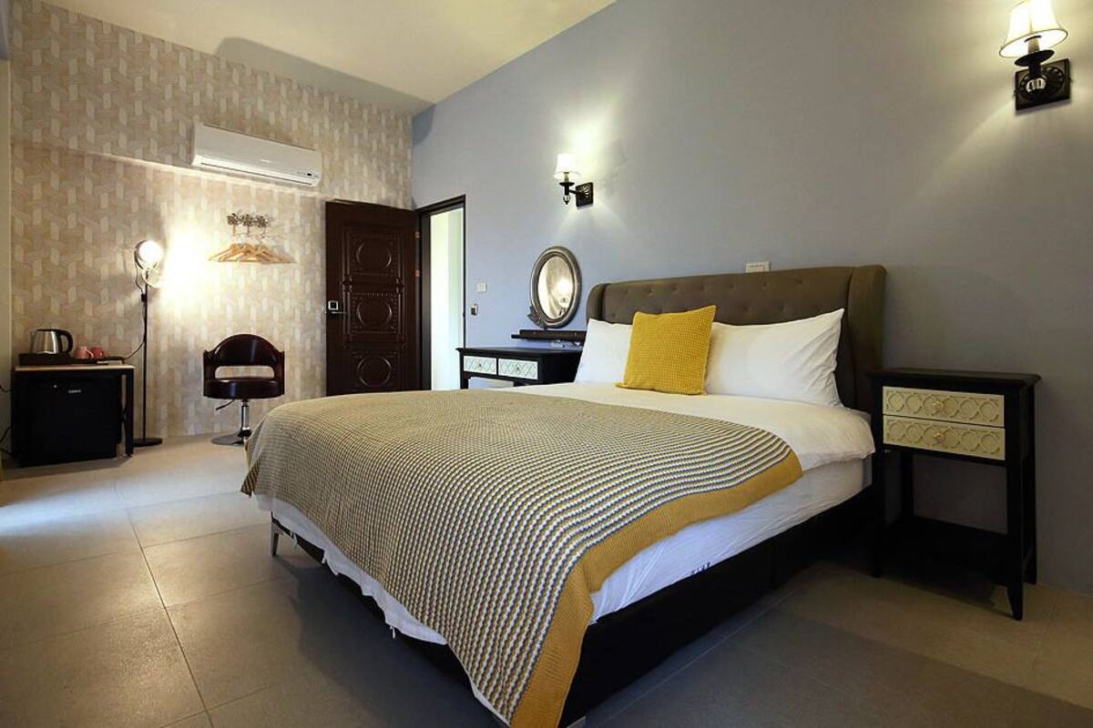 A hotel room with a large bed, bedside tables, a mirror, an air conditioning unit, and a lamp.