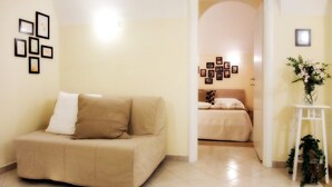 A cozy room with a beige sofa, a bed with a white headboard, and a small white table with a plant. - La Chiostrina (Rome)