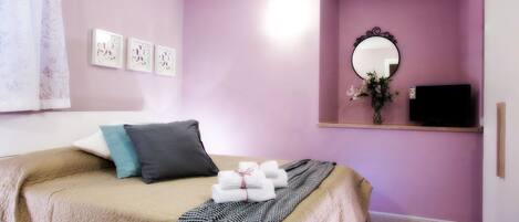 Un dormitorio con cama, almohadas, una colcha, un espejo y obras de arte en la pared.