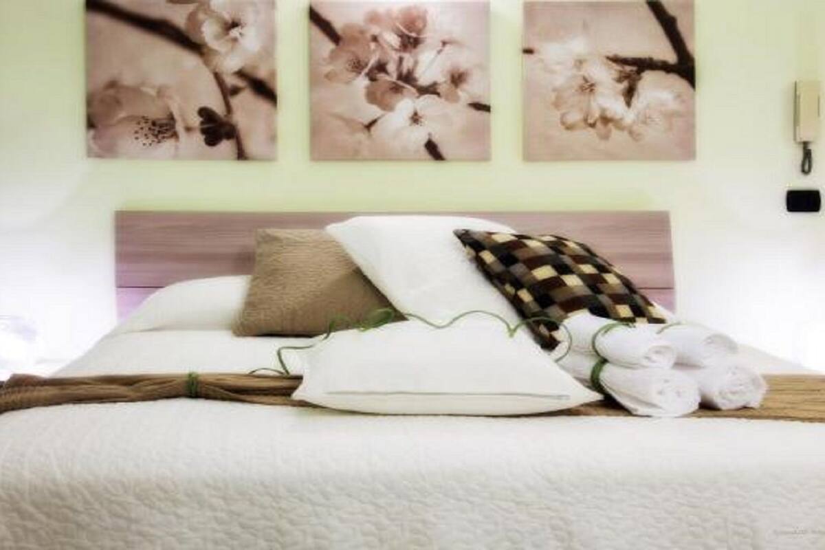 A neatly made bed with pillows and a blanket, a wall-mounted phone, and three floral paintings above the bed.