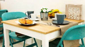 A dining table with a plate of croissants, a metal bucket with flowers, a blue cup, and a fruit basket. - La Chiostrina (Rome)