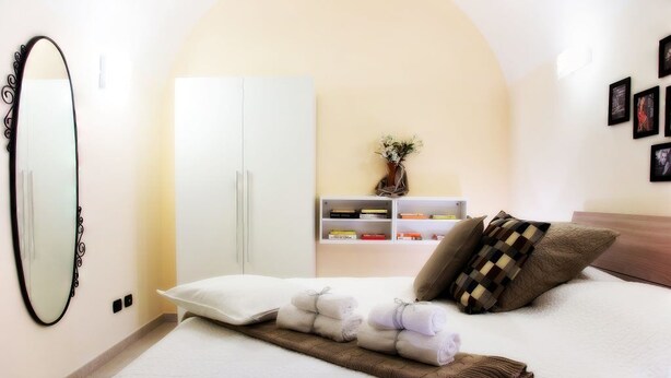 A neatly made bed with pillows and towels, a wardrobe, a shelf with books and a vase, and a mirror on the wall. - La Chiostrina (Rome)