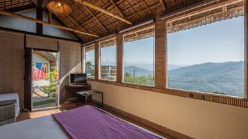 A room with a bed, a desk, a TV, and large windows offering a view of mountains.