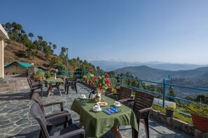A terrace with tables set for dining, overlooking a mountainous landscape. - Heritage Resort (Garur)