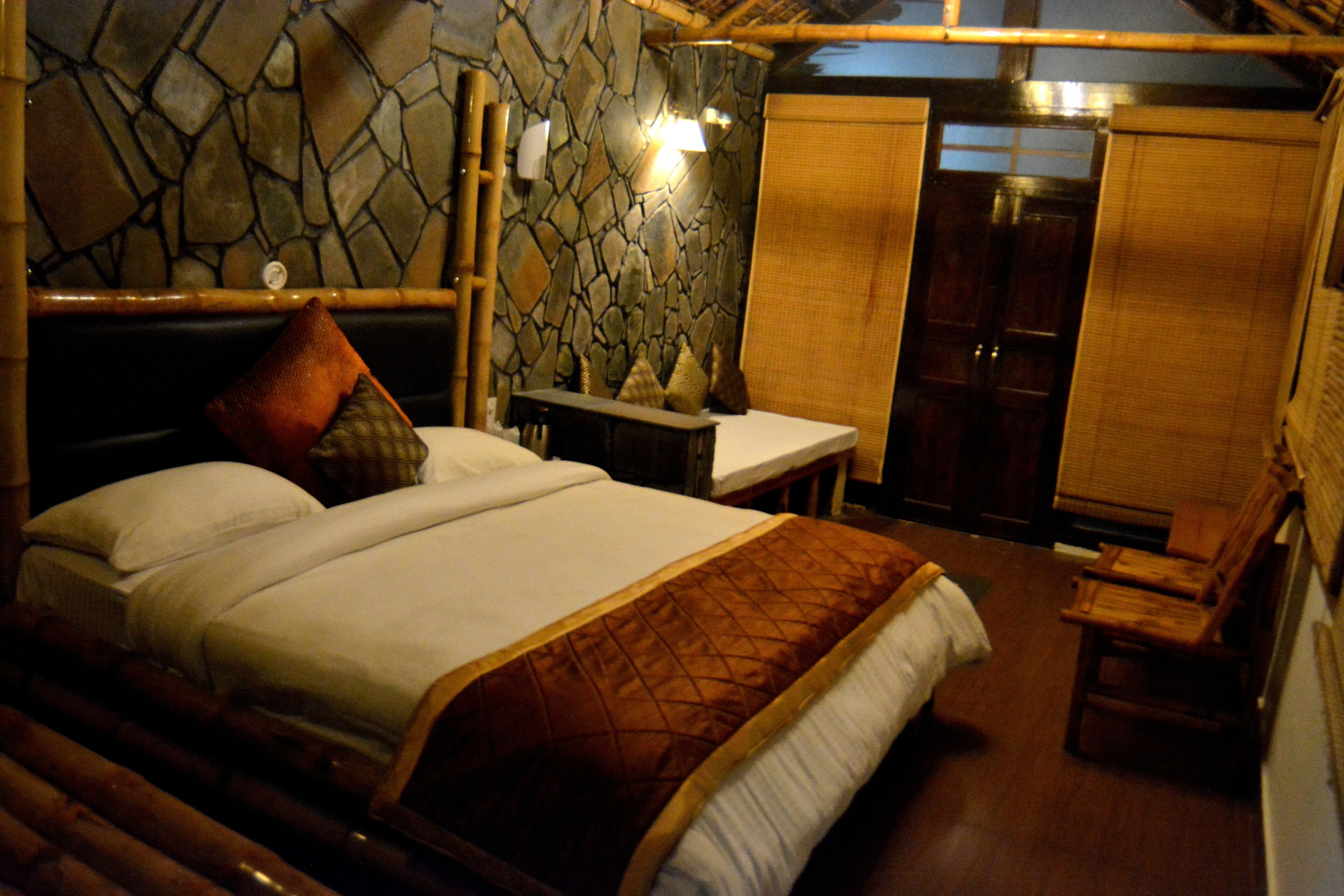 A room with a bed, a wooden bench, a table, and a stone wall.