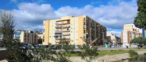 A multi-story residential building with balconies, a small pond, and surrounding greenery.