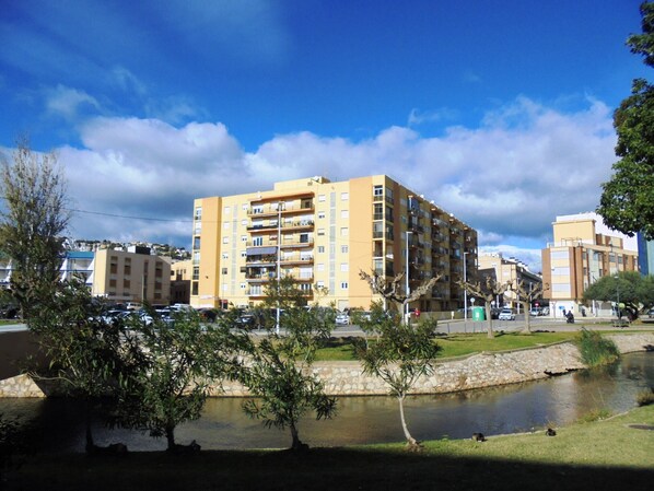 Un immeuble résidentiel à plusieurs étages, doté de balcons, d’un petit étang et entouré de verdure.