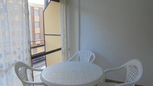 A small balcony with a white table and two chairs, a patterned curtain, and a view of a building with balconies. - Los Labradores (Peñiscola)