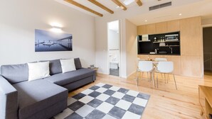 A modern living room with a grey sofa, a checkered rug, and a kitchen area with white chairs and wooden cabinets. - Freixo - River View Apartment (Oporto)
