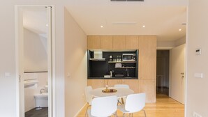 A modern kitchen with white cabinets, a black countertop, and a dining area with a white table and chairs. - Freixo - River View Apartment (Oporto)