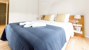 A hotel room with a large bed, white walls, wooden ceiling beams, and a wooden floor. - Freixo - River View Apartment (Oporto)