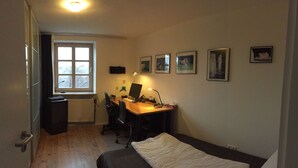 Una habitación pequeña y con pocos muebles, que incluye un escritorio de madera, una computadora, una silla, un radiador, una ventana y una cama.