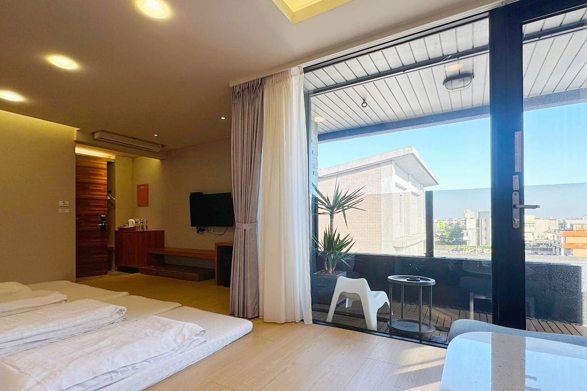 Habitación de hotel con una cama grande, televisión, escritorio y balcón con vista a la ciudad.