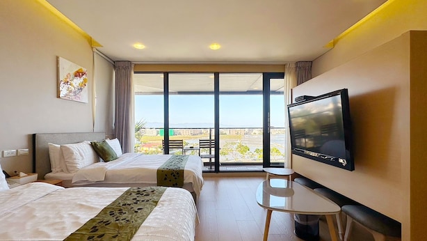 Habitación de hotel con dos camas, televisión, una mesita y balcón con vistas.