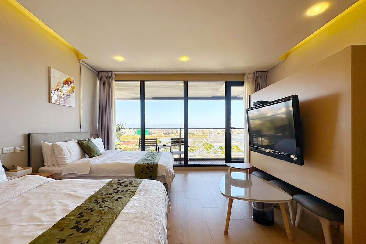 Habitación de hotel con dos camas, televisión, una mesita y balcón con vistas.