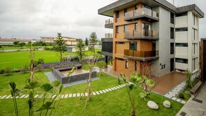 Un edificio moderno de varios pisos con balcones, un patio con vegetación y un césped bien cuidado.