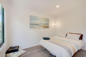 A bedroom with a bed, a painting, a lamp, and a window.