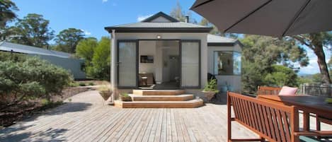 Une maison moderne dotée d’une terrasse, d’un coin repas avec une table et des chaises, et d’un grand parasol.