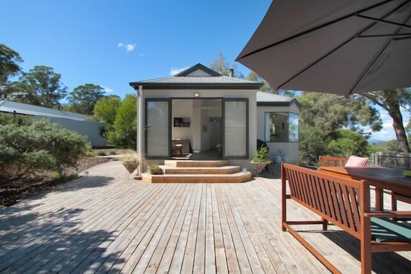 A modern house with a deck, a dining area with a table and chairs, and a large umbrella.