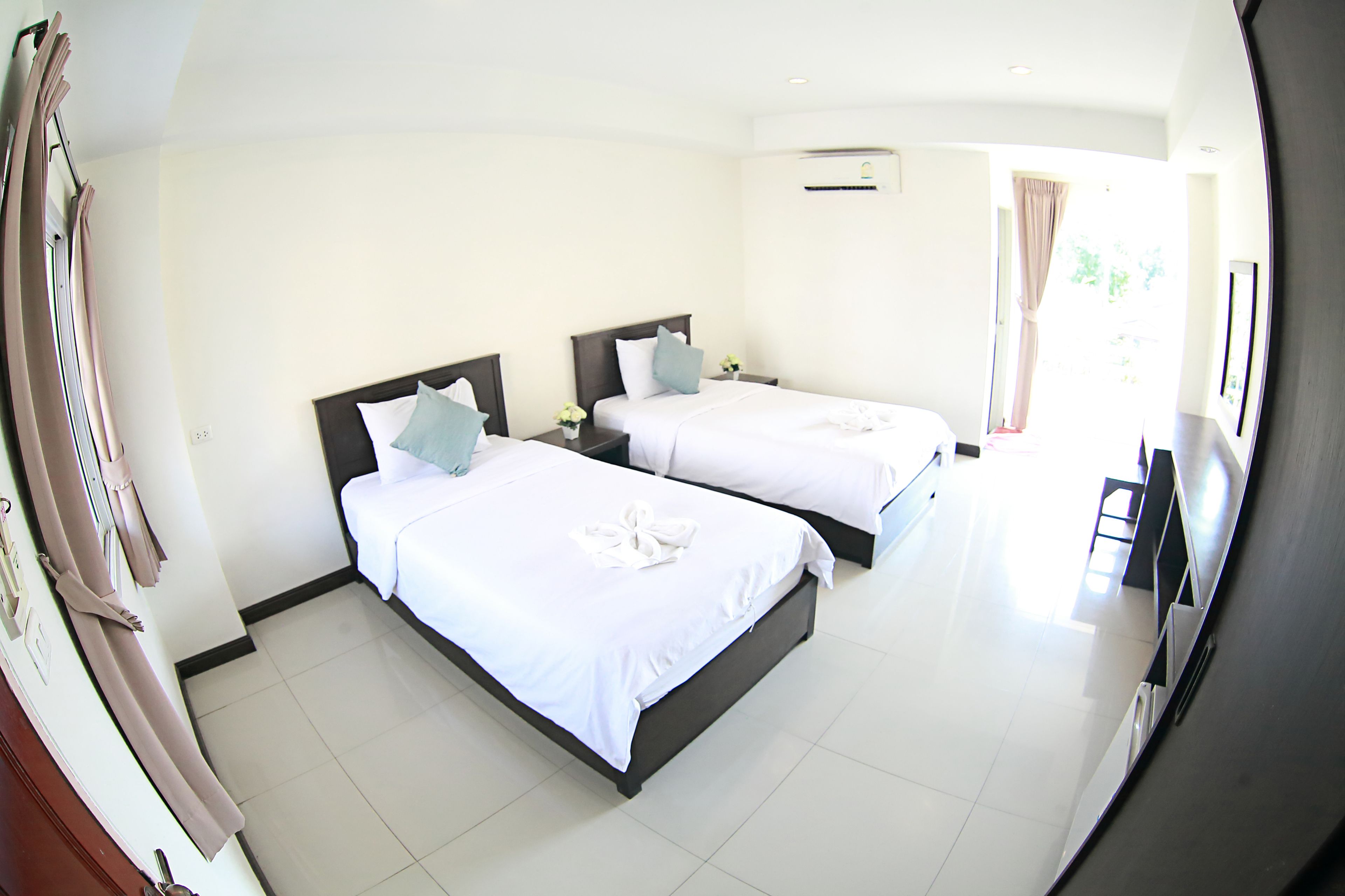 A hotel room with two beds, a flat-screen TV, and a window with curtains.