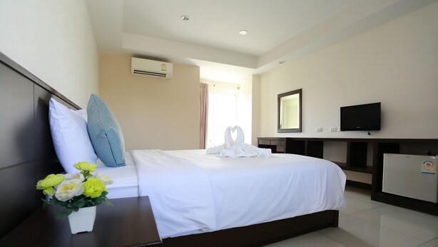 A hotel room with a bed, a small table with a vase of flowers, a television, and a minibar. - Weerawan Place (Khon Kaen)