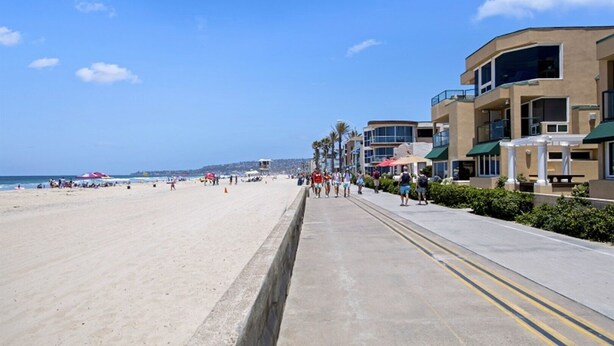 A beach with a concrete walkway, palm trees, and buildings with balconies. - Affordable and ocean front! (San Diego)