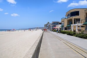 A beach with a concrete walkway, palm trees, and buildings with balconies. - Affordable and ocean front! (San Diego)