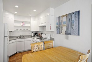 Uma cozinha moderna com armários brancos, uma mesa de jantar de madeira e uma pintura com paisagem costeira.