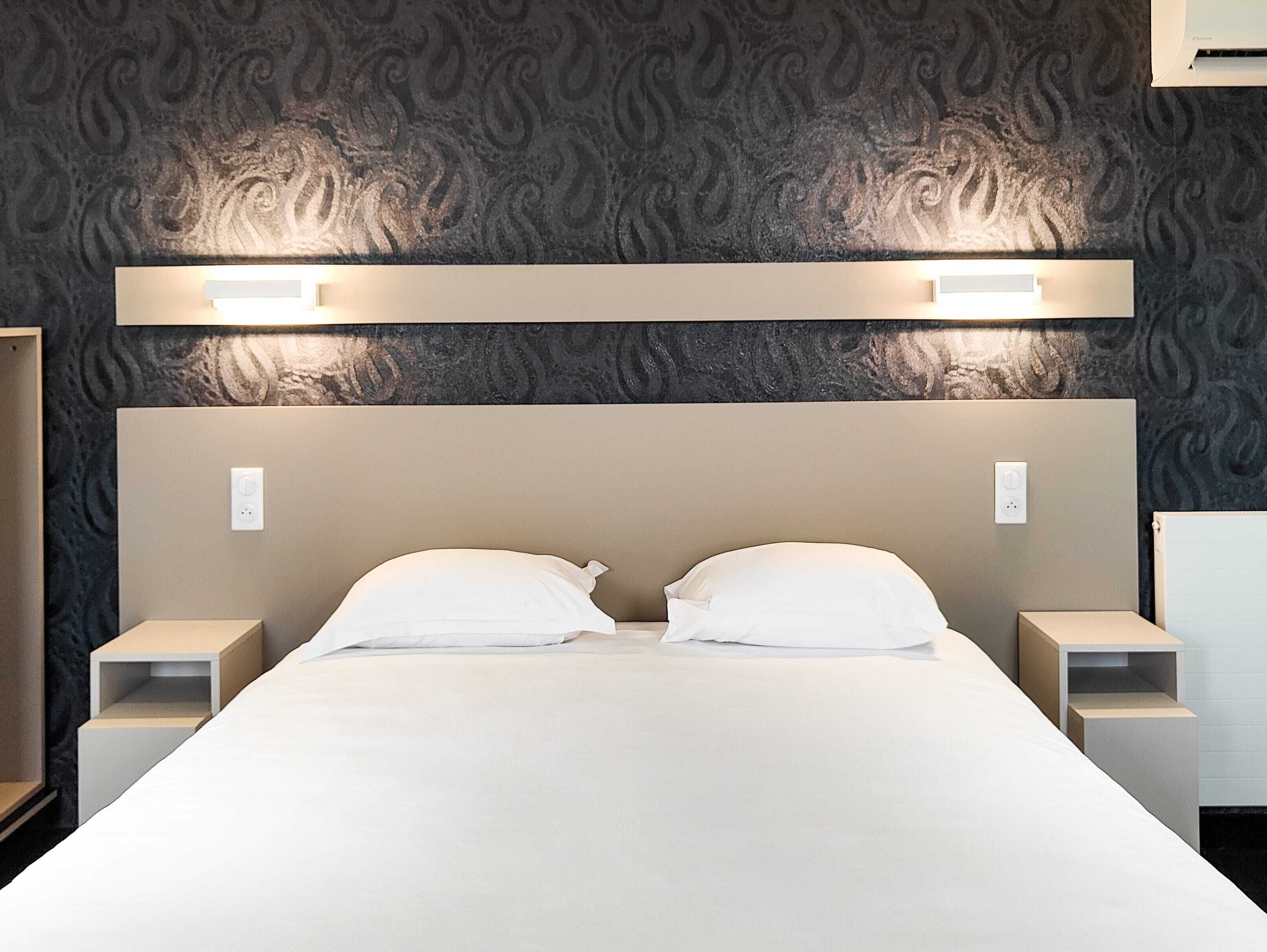 A hotel room with a large bed, two bedside tables, and a headboard with built-in lighting.