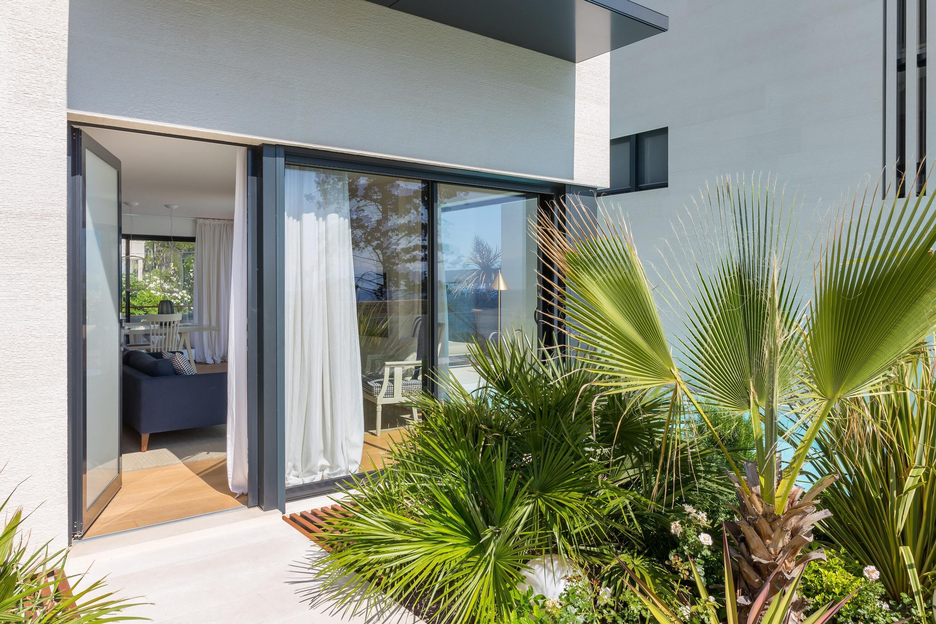 Une maison moderne dotée d’une porte vitrée donnant sur un patio agrémenté de plantes et d’un espace salon.
