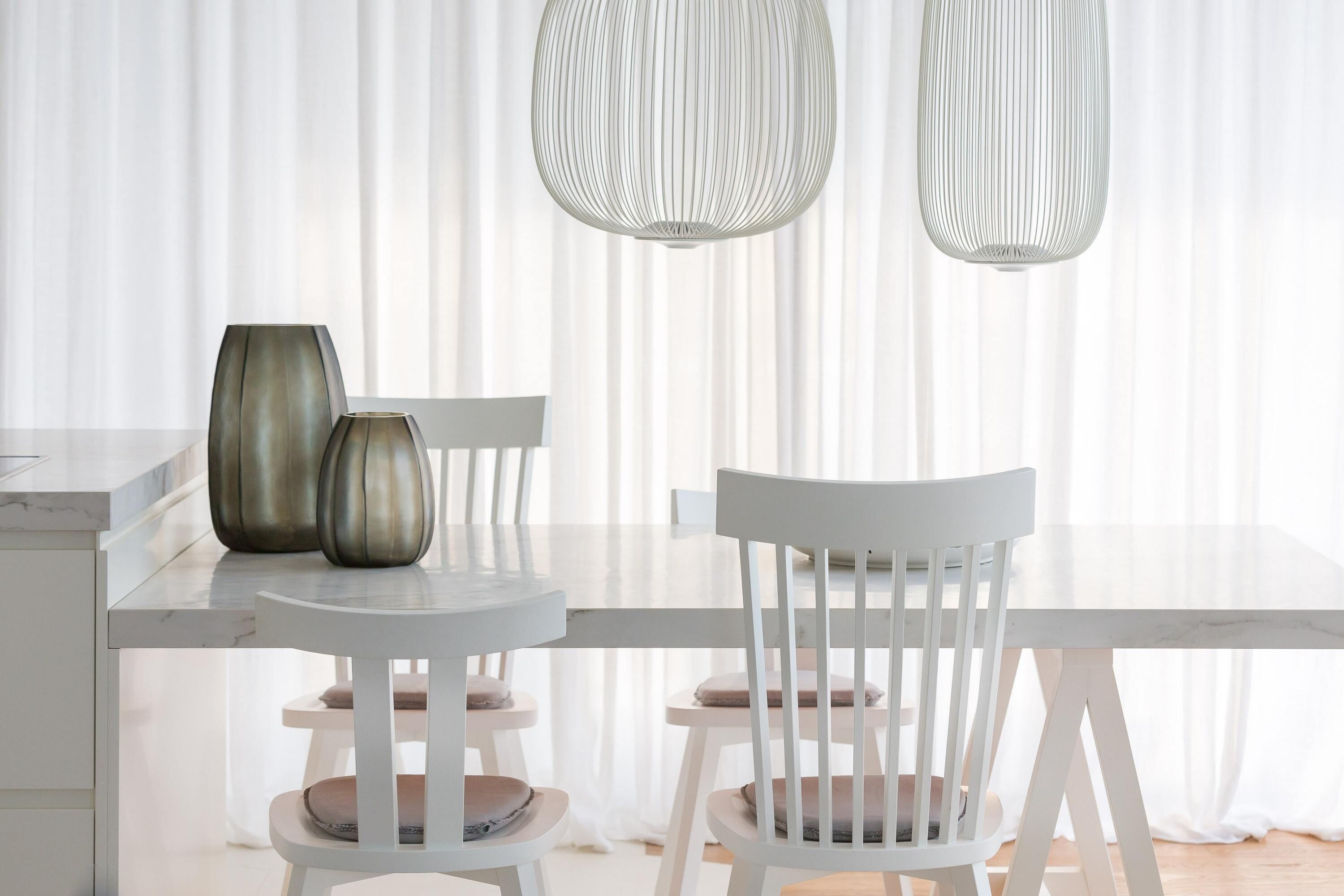 A dining area with a white table and chairs, two vases, and a hanging light fixture.
