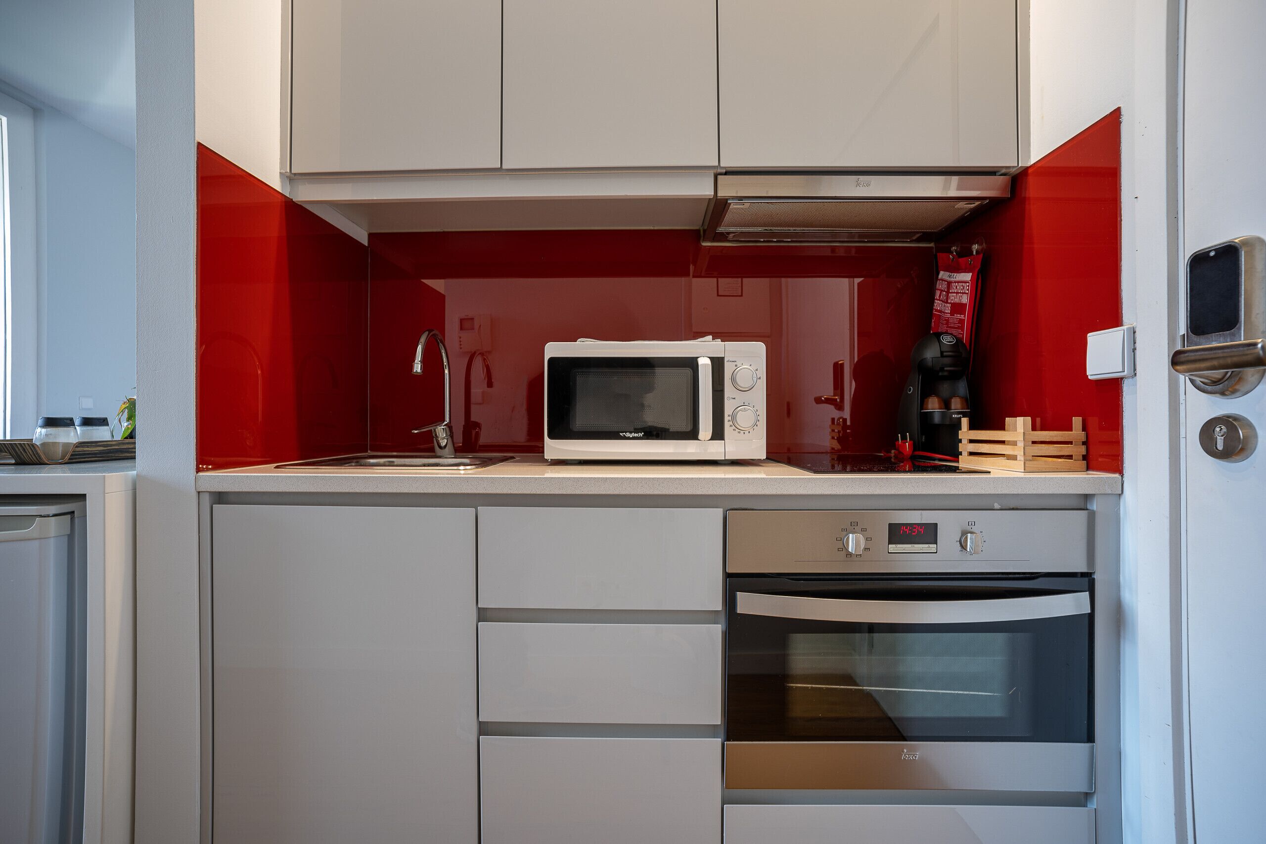Une cuisine de taille réduite équipée d’un four à micro-ondes, d’un four traditionnel et d’un mur d’accent de couleur rouge.