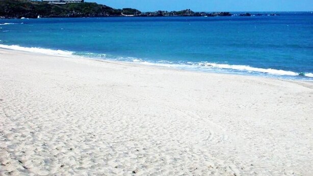Ein Strand mit weißem Sand und klarem, blauem Wasser.