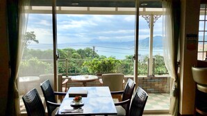 Ein Essbereich mit Tisch und Stühlen, Blick auf das Meer und die Berge sowie ein Balkon mit Geländer.