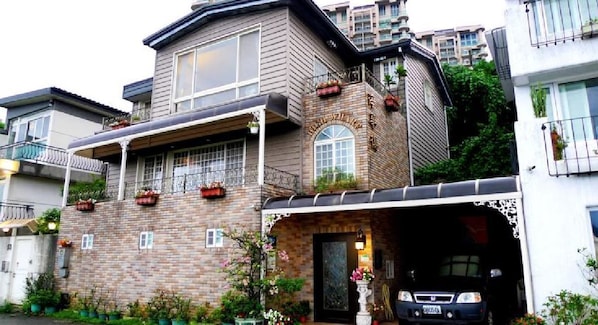 A two-story house with a garage, brick exterior, and a balcony with potted plants.