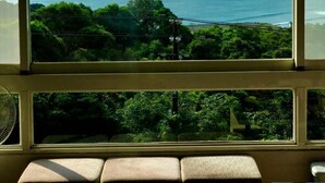 Ein Zimmer mit großem Fenster und Blick auf die Küstenlandschaft, einer gepolsterten Sitzbank und einem kleinen Tisch mit einem dekorativen Gegenstand.