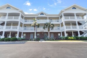 A multi-story hotel with balconies, a central entrance, and palm trees.