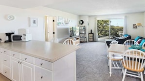 A modern kitchen with white cabinetry, a microwave, and a dining area with a table and chairs.