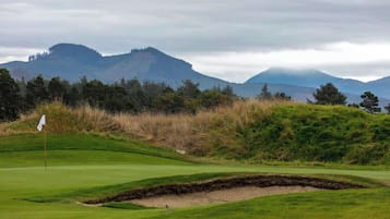 Ein Golfplatz mit Fahne, Bunker und einem Bergpanorama.