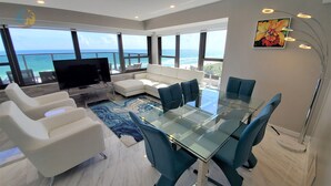 Un salon moderne avec une table à manger en verre, des canapés blancs et un grand téléviseur.