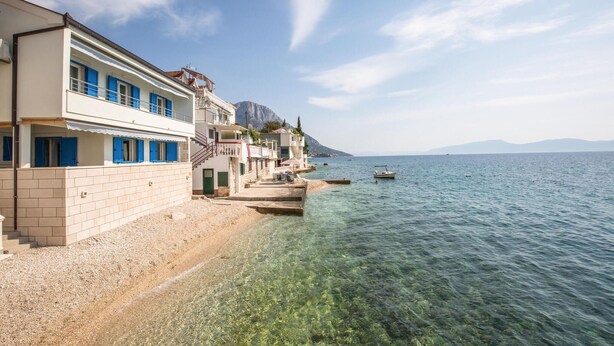 A coastal building with a clear view of the sea, a sandy beach, and a mountainous backdrop.