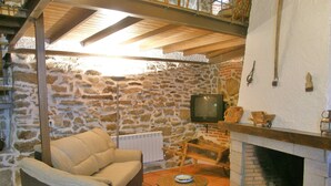 A cozy living room with a stone wall, a fireplace, a sofa, a television, and a small table. - Cozy Cottage with Jacuzzi for 8/10 people.  (Navalosa)