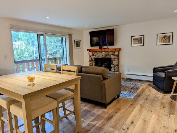 Een woonkamer met een stenen openhaard, een daarboven bevestigde televisie, en een balkon met uitzicht op bomen.