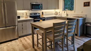 Une cuisine moderne équipée d’appareils électroménagers en acier inoxydable, une table à manger en bois et une fenêtre donnant sur la verdure.